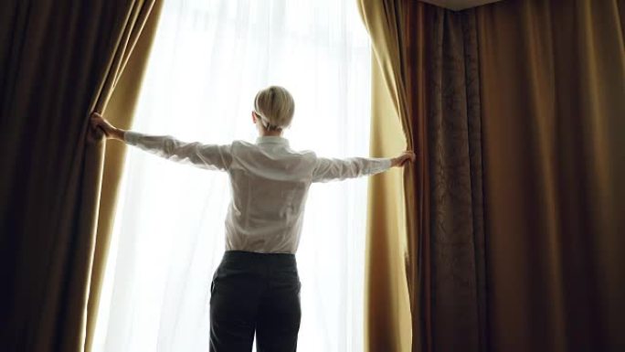 女商人早上在酒店房间里揭开窗帘，看着窗户