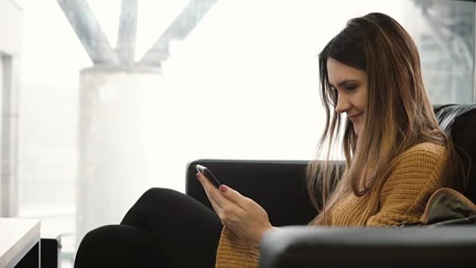 年轻的黑发女人坐在靠近窗户的咖啡馆里，使用智能手机。迷人的女性在互联网上聊天