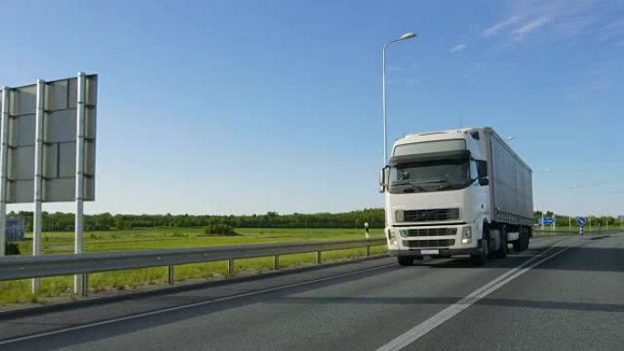 大型白色半卡车，带货运拖车，在工业区空旷的道路上行驶，背景是阳光普照。