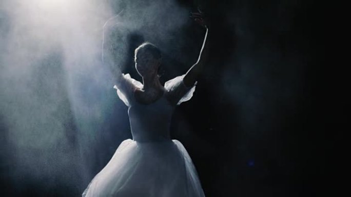 一位美丽的年轻芭蕾舞演员在聚光灯下优雅地旋转。她向空气中投掷灰尘颗粒，它们在她周围的黑暗中发光。她穿