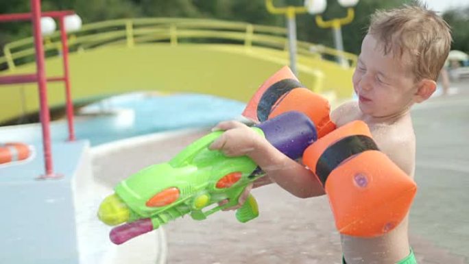 慢动作特写: 小男孩玩水仗，开枪打死他的父亲，他在阳光明媚的夏天在有趣的水上公园被溅回