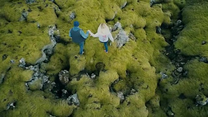 这对年轻美丽的夫妇走在覆盖着苔藓的火山岩上，探索大自然的顶部鸟瞰图
