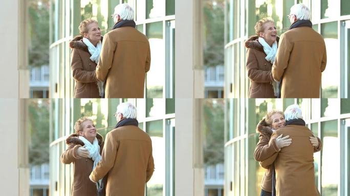 穿着大衣的老年情侣在大楼外聊天，拥抱