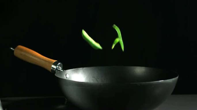 切成薄片的青椒落入黑色背景的炒锅中