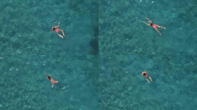 空中: 女孩屏住呼吸，淹没，在透明的海水中游泳