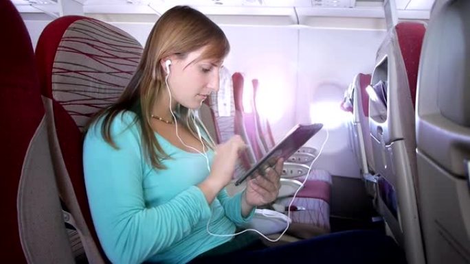 在飞机上使用数字平板电脑的年轻女子