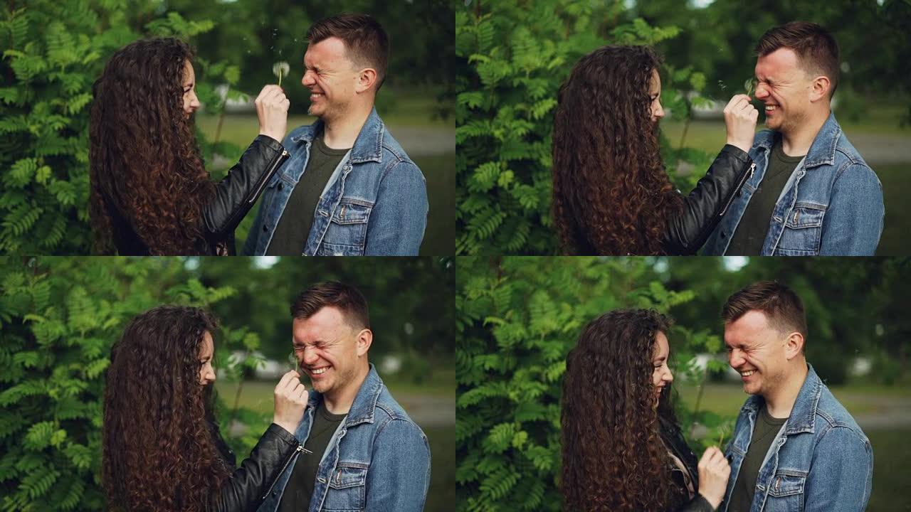 两个有吸引力的人的慢动作快乐的恋人玩蒲公英吹气球在周末在公园里玩得开心并大笑。夫妻和自然概念。