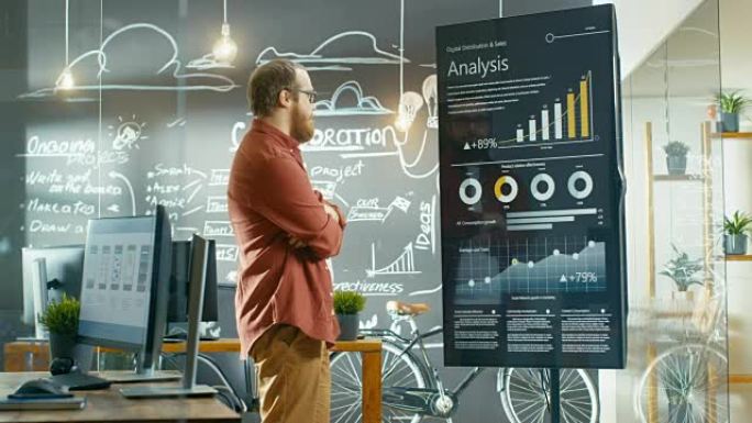 Marketer查看交互式触摸屏白板，显示有关统计增长的最新图形和图表。他在创意办公室工作。