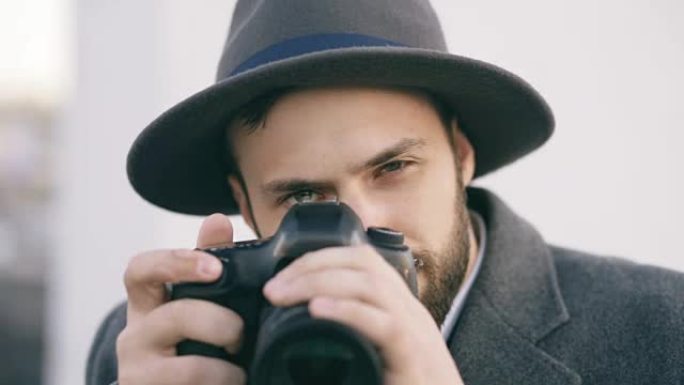 一个可疑的年轻摄影师在给你拍照。潮男间谍的概念，戴着帽子拍照和看着相机