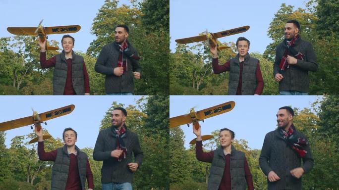 父子俩在向摄像机奔跑时正在公园里发射飞机模型。慢动作。