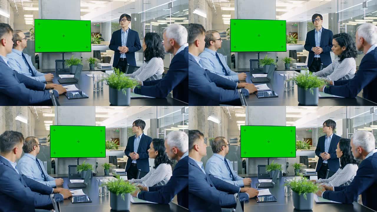 亚洲商人向他的业务同事提供报告/演示，指向指向绿色色度键屏幕墙电视的结果。