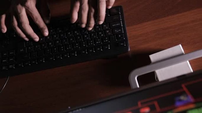 顶视图。在黑暗的房间里，男人用手在键盘上打字。黑客，it专业人员，工作中的计算机专家。无法辨认