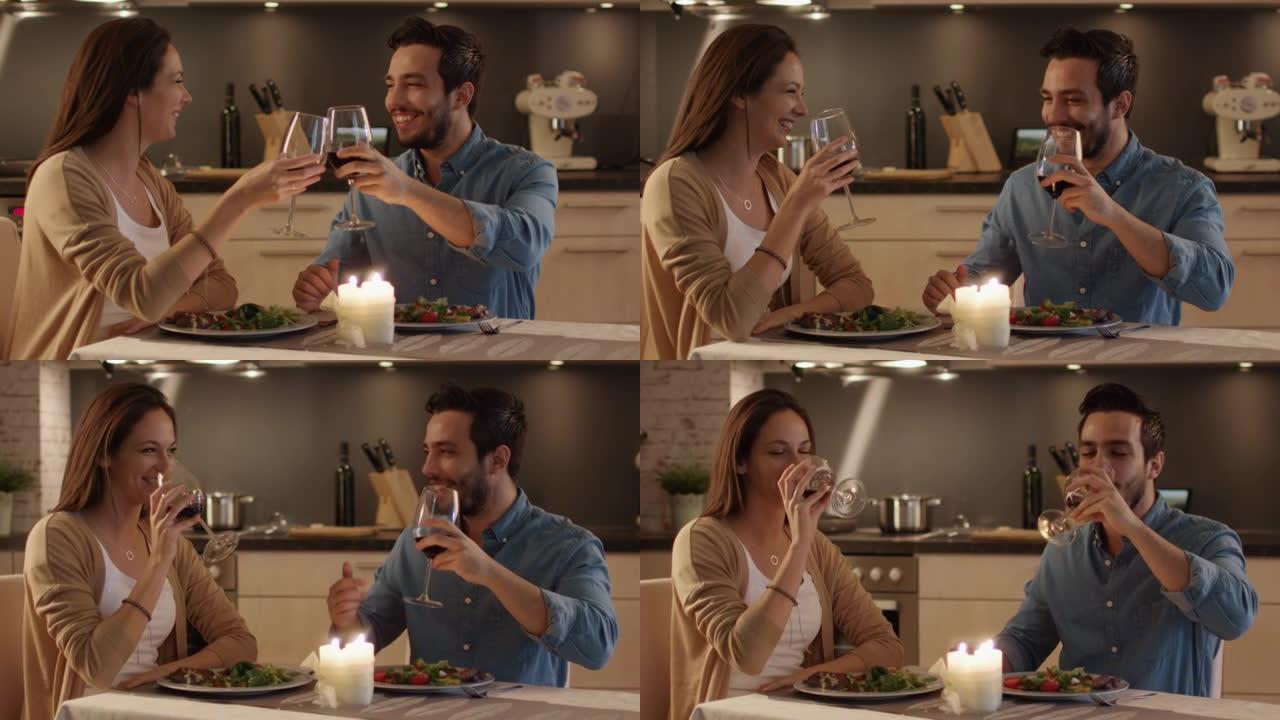 美丽的夫妇在厨房吃烛光晚餐。他们吃饭、喝酒和说话。为了庆祝他们碰杯。