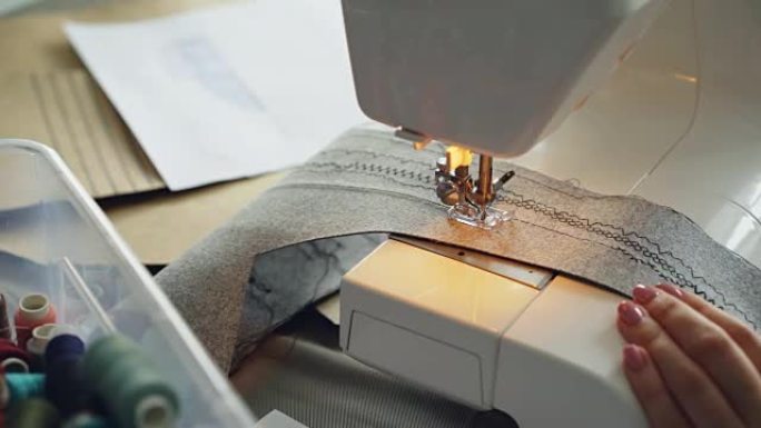 现代电动缝纫机拼接纺织品的特写镜头。女孩修剪整齐的手和五颜六色的缝纫线可见。