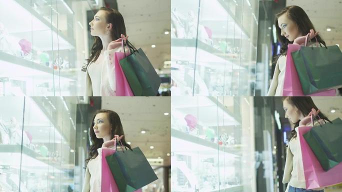 带着购物袋的年轻漂亮女孩正在购物中心珠宝店的橱窗里看。手持镜头