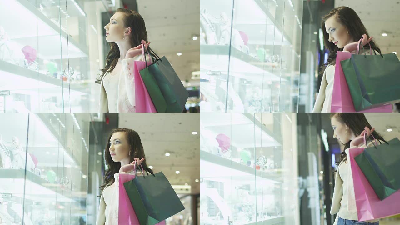带着购物袋的年轻漂亮女孩正在购物中心珠宝店的橱窗里看。手持镜头
