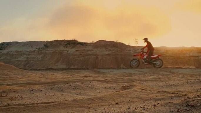 侧面拍摄的专业自行车骑手驾驶他的FMX摩托车在桑迪越野赛道上。风景优美的日落是背景。