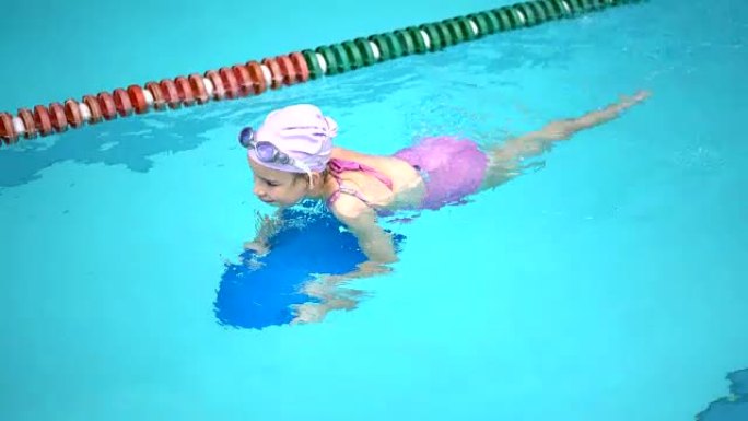 游泳池里的小女孩学习使用游泳板游泳