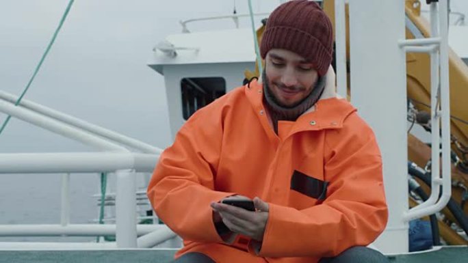 在船上旅行时，穿着随意的渔夫使用手机。