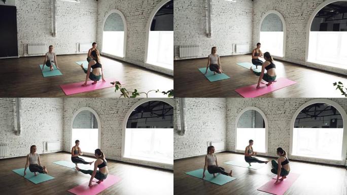 经验丰富的瑜伽老师正在健康中心向两名女学生展示平衡姿势。白色的墙壁，明亮的垫子，大窗户可见。