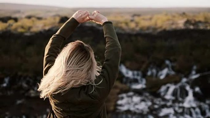 年轻的金发女子站在冰岛的巴纳福斯瀑布附近，欣赏美丽的风景