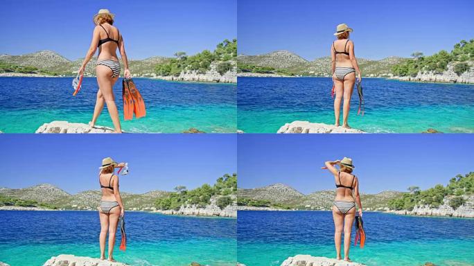 穿着比基尼的女人在阳光明媚的夏日蓝色海洋中拿着浮潜护目镜和鳍状肢