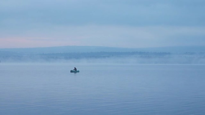 雾蒙蒙的森林湖上的渔夫。