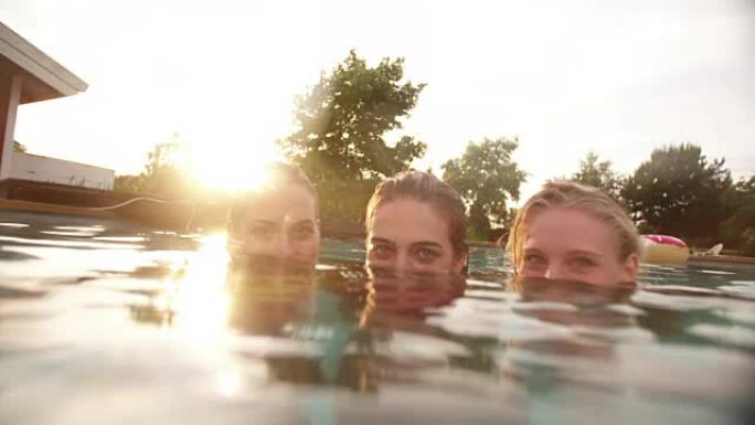 日落时淹没在游泳池中的三个女孩的肖像