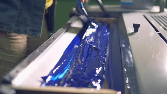 一名员工正在打印托盘中的蓝色油漆上传递刷子