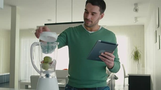 英俊的男人正在厨房里使用平板电脑时准备冰沙。