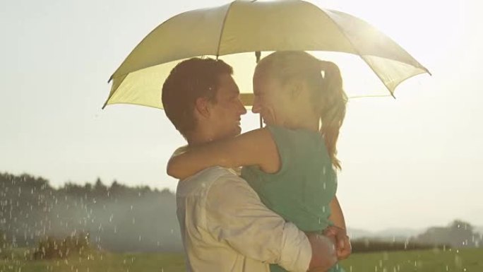 镜头耀斑: 浪漫约会的年轻男女在黄色雨伞下旋转。