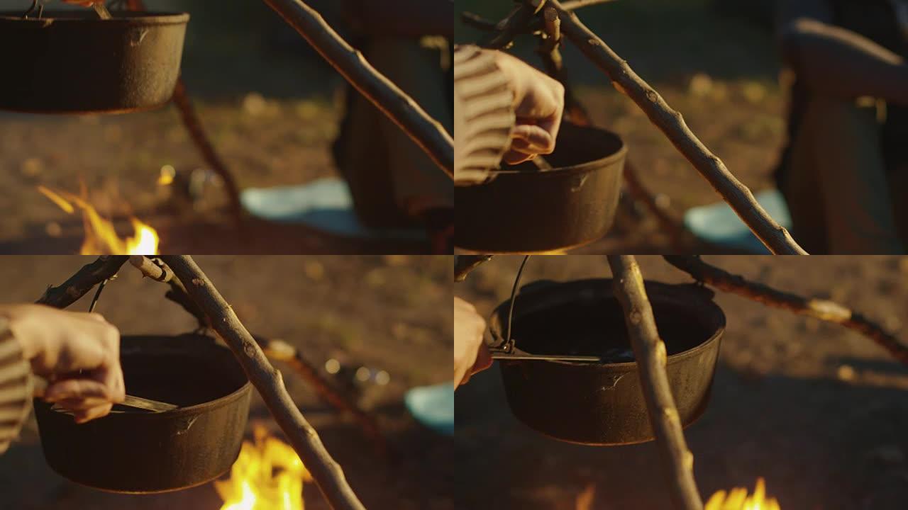 男人的手搅动在晴天在篝火上准备的沸水。