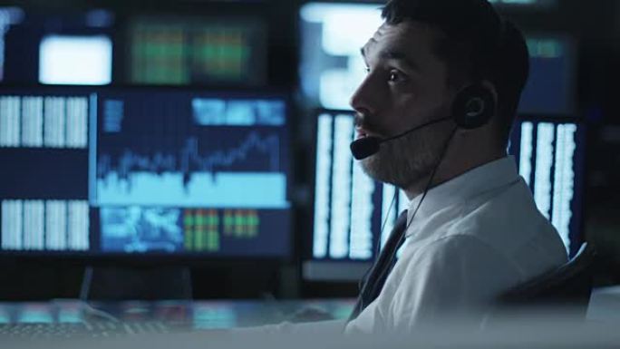 在一间满是显示屏的黑暗办公室里，一名股票经纪人一边用耳机说话，一边在电脑上工作。