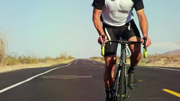 在阳光明媚的日子里，在沙漠路上外面的公路自行车上骑自行车的人的慢动作特写