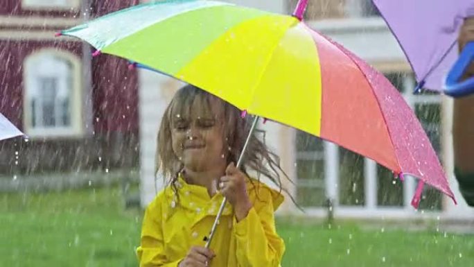 穿着黄色雨衣的可爱女孩在雨中跳跃