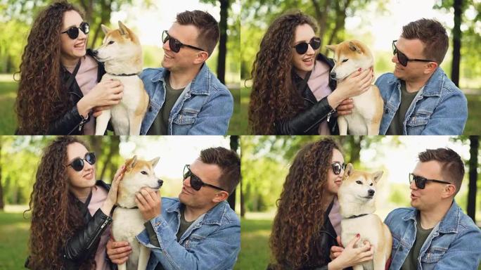 骄傲的狗主人漂亮的女孩和帅哥正在和柴犬一起玩，亲吻它，并在周末在公园里抓挠它的皮毛。人和动物的概念。