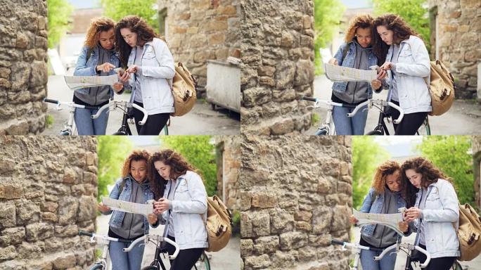 失落的游客漂亮女孩看着纸质地图和智能手机屏幕站在街上，骑着自行车寻找旅游目的地。