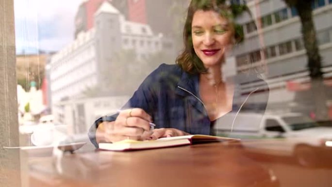 时髦的女人在咖啡店的靠窗座位上写日记