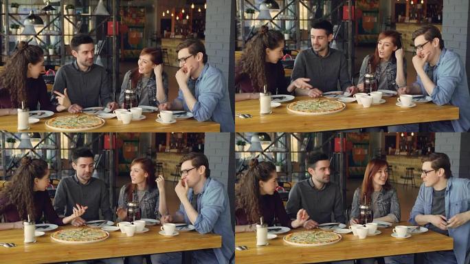 开朗的年轻朋友坐在现代咖啡馆的餐桌旁聊天和打手势分享新闻。可以看到大披萨，杯子和盘子，桌子和椅子。