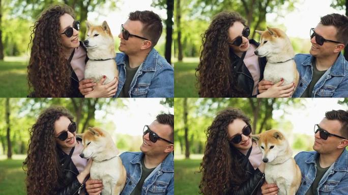 快乐的人的慢动作亲吻和爱抚可爱的狗触摸它的皮毛，而动物正在享受爱和关怀。年轻的家庭正在公园里度过空闲