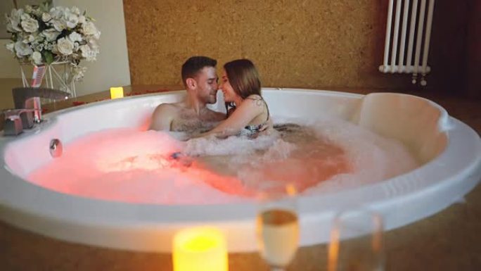 年轻的大胡子男人和他迷人的女友在浴缸里聊天，拥抱和大笑。浪漫关系、健康和幸福的人的概念。