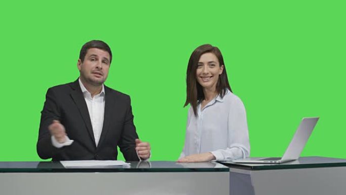 男女广播公司坐在桌子旁，在后台的模拟绿屏上聊天。