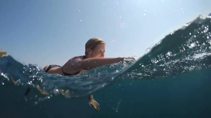 慢动作，半水下: 微笑的女孩躺在冲浪板上划出