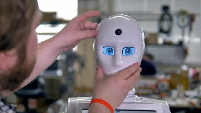 一位工程师在机器人脸上戴上白色面具。