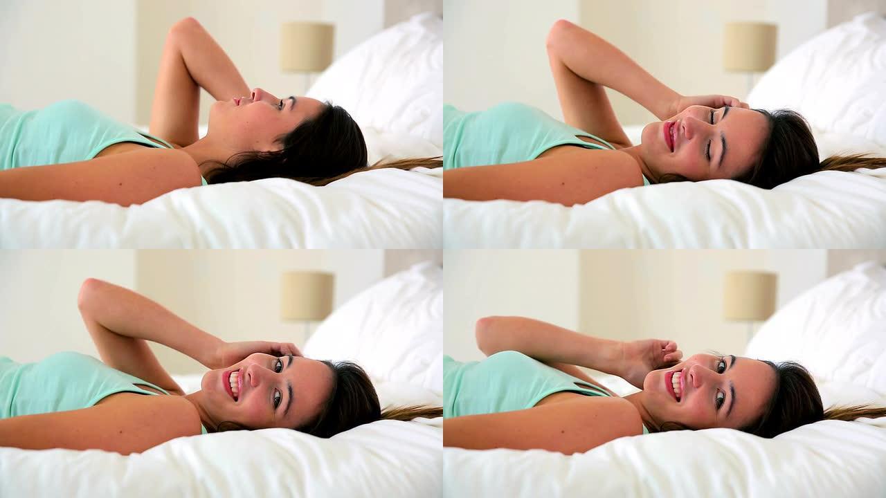 漂亮的黑发女人躺在床上对着镜头微笑