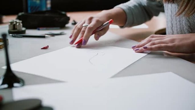 女人坐在办公室的桌子旁，拿着铅笔在纸上画鞋子的草图。滑块右侧，侧视图。4K