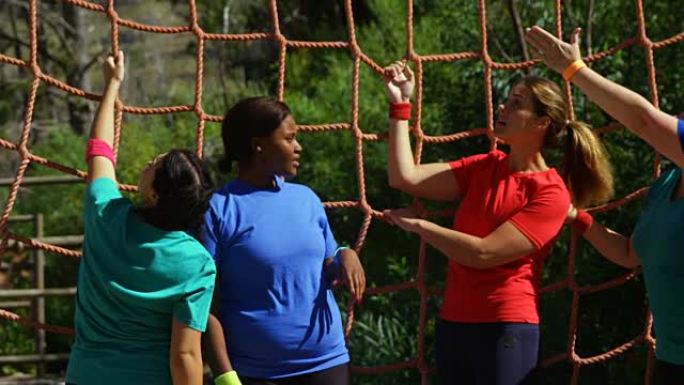 女教练在障碍赛中协助妇女攀爬网