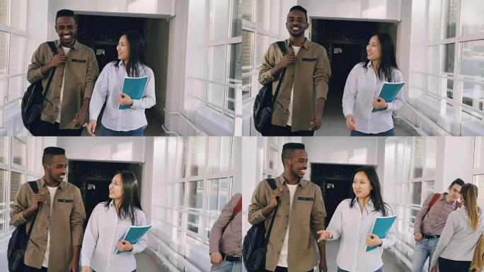 年轻的有吸引力的非洲男性和亚洲女学生正在走廊上移动，讨论一些生动活泼的事情，并示意另一对站在高窗附近