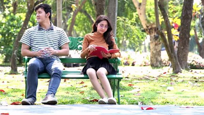 夫妇坐在秋天公园的长凳上。年轻的夫妇坐在户外公园日光浴，放松，微笑，打哈欠，看书