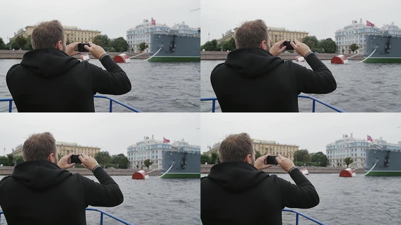 圣彼得堡观光。男人使用智能手机，拍摄巡洋舰Aurora的照片，在船上经过它，慢速